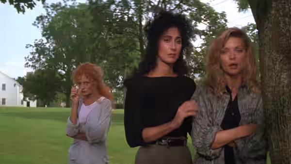 Alexandra Medford (Cher), Jane Spofford (Susan Sarandon) and Sukie Ridgemont (Michelle Pfeiffer) stand together on a lawn