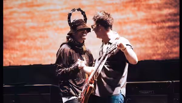 Two guitarists facing each other closely on a lit stage