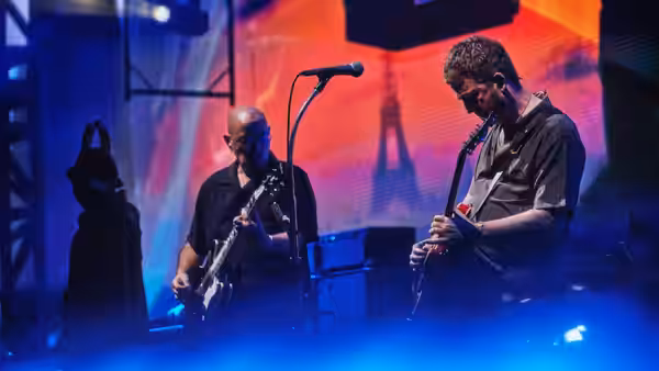 Two guitarists play on stage with an illuminated Eiffel Tower screen behind them