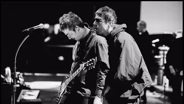 Liam Gallagher and Noel Gallagher playing guitars side by side on stage