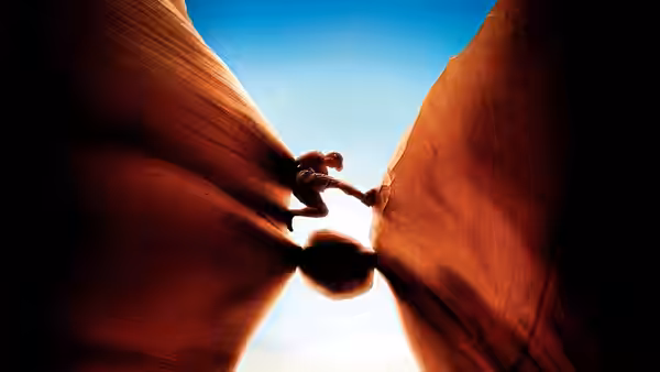 a climber wedged between towering canyon walls under blue sky
