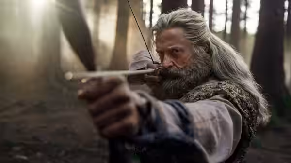 Robin Hood (Hugh Jackman) aiming a bow in a sunlit forest