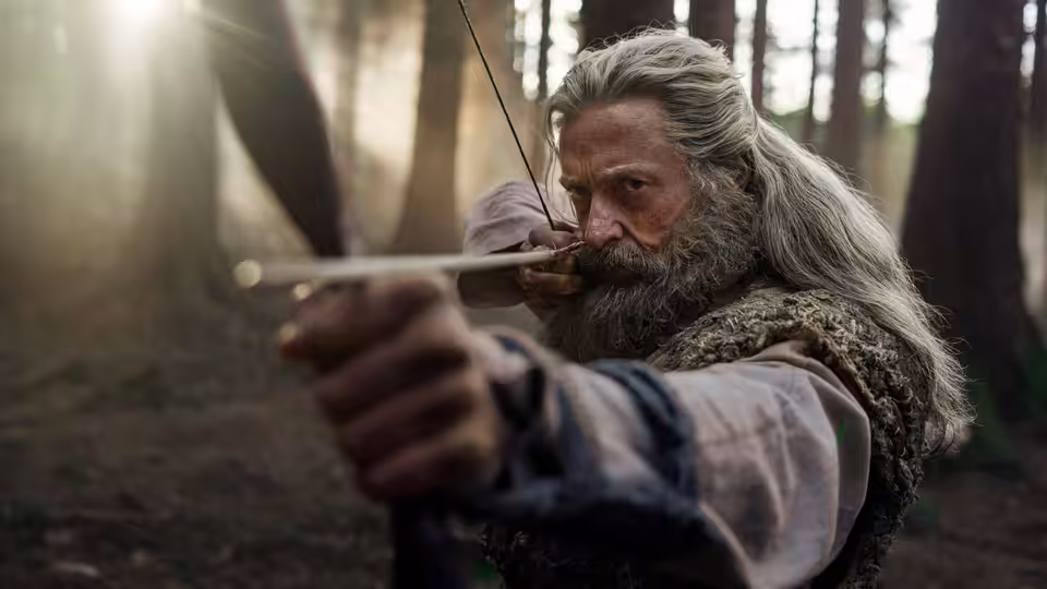 Robin Hood (Hugh Jackman) aiming a bow in a sunlit forest