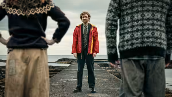 a man in a red jacket stands on a concrete pier facing two others