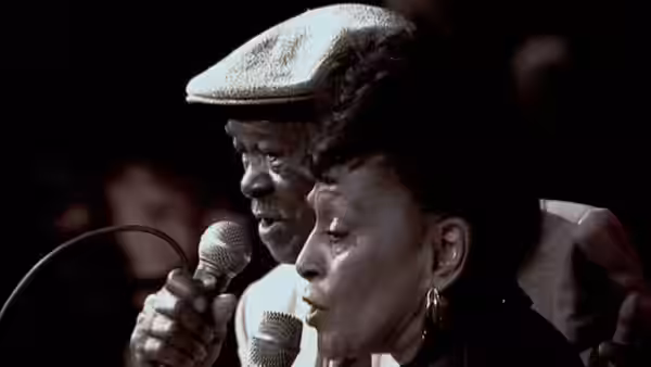 Man and woman singing together into microphones on a dark stage