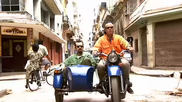Two men riding a blue motorcycle with sidecar through a narrow street