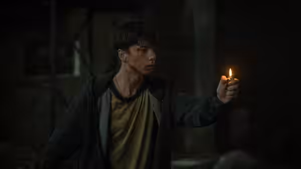 Naim Reid (Joe Bird) holding a lit candle inside a dark derelict building