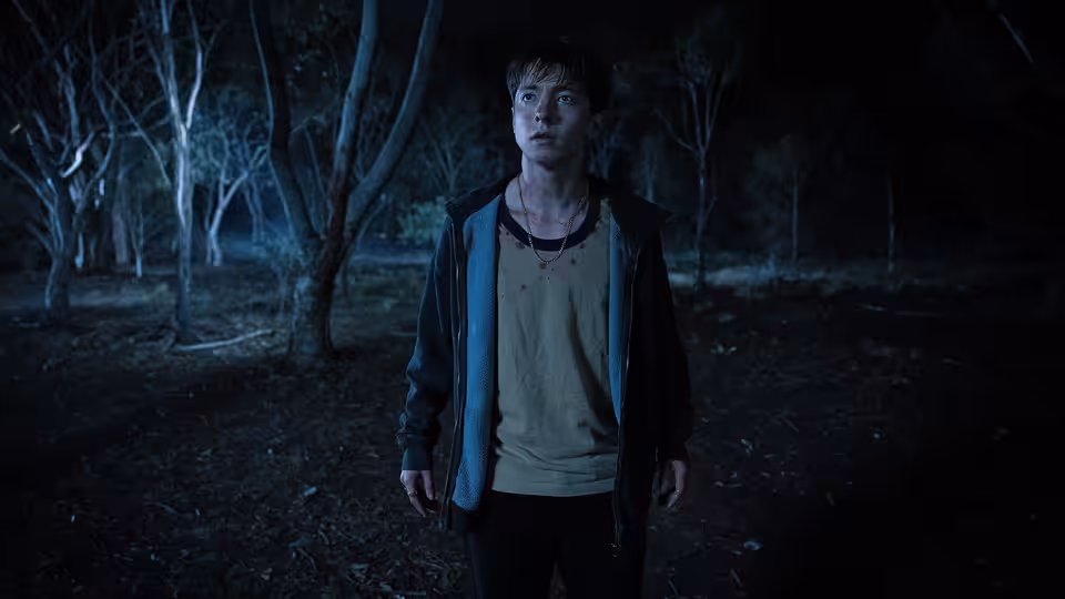 Naim Reid (Joe Bird) standing alert in a dark wooded area at night