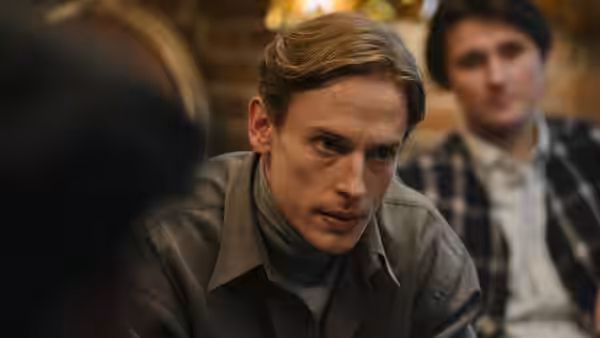 A young man in a leather jacket leaning forward with focus