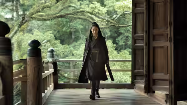 Nie Yinniang (Shu Qi) walking on a wooden veranda overlooking trees