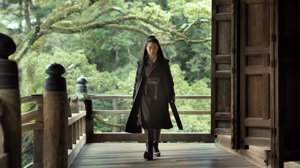 Nie Yinniang (Shu Qi) walking on a wooden veranda overlooking trees