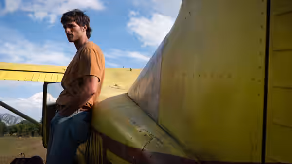 Hig (Jacob Elordi) leaning against a yellow airplane in a field