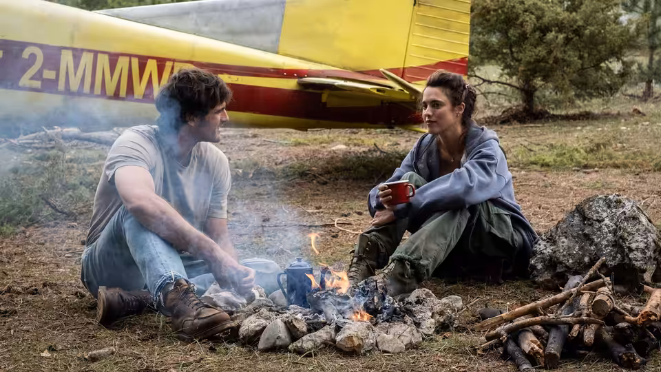 Hig (Jacob Elordi) and Cima (Margaret Qualley) sitting by a campfire near a plane