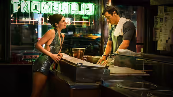 Allie (Monica Barbaro) leaning on counter as Owen (Callum Turner) works behind it