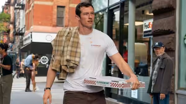 Owen (Callum Turner) carrying pizza boxes along a city sidewalk