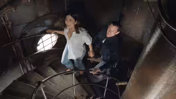 Allie (Monica Barbaro) and Owen (Callum Turner) climbing a metal spiral staircase