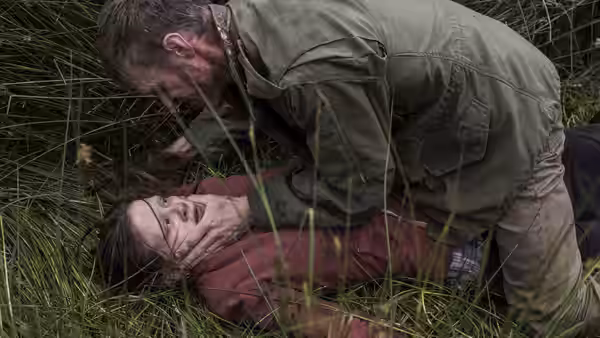 The Survivalist (Martin McCann) restrains another person in the grass