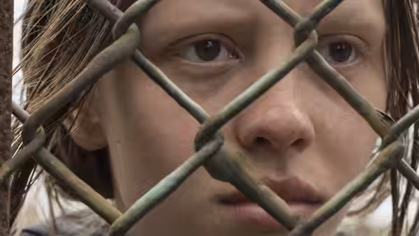 Milja (Mia Goth) peers through a chain-link fence