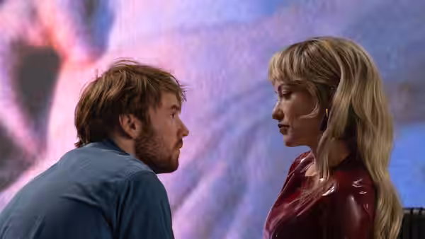 A bearded man and a blonde woman gaze intently at each other