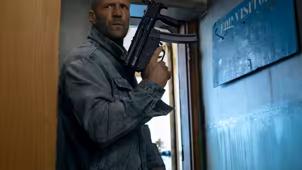 Cole Reed (Jason Statham) holding a submachine gun in a doorway