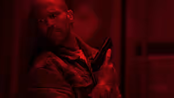 Cole Reed (Jason Statham) holding a handgun in red lighting