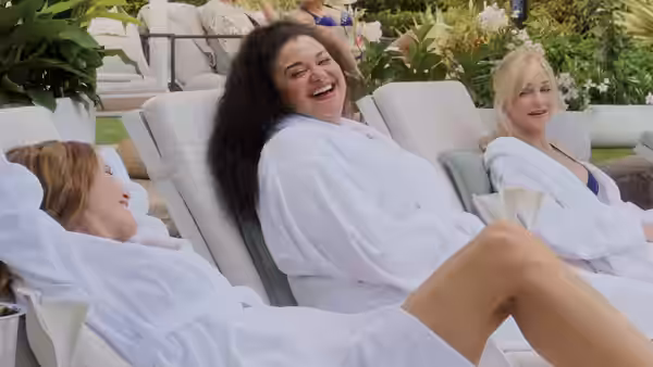 Three women in white robes laughing on outdoor lounge chairs