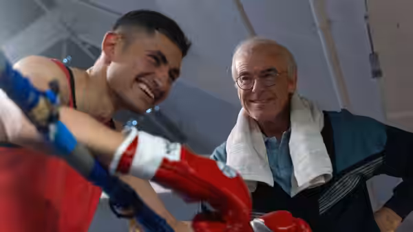 Naz (Amir El-Masry) smiles beside Brendan Ingle (Pierce Brosnan) in the gym