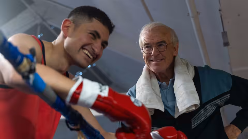 Naz (Amir El-Masry) smiles beside Brendan Ingle (Pierce Brosnan) in the gym
