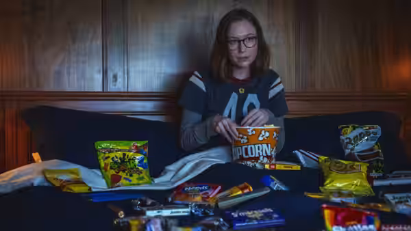 Kris sitting on a bed holding popcorn among scattered snacks