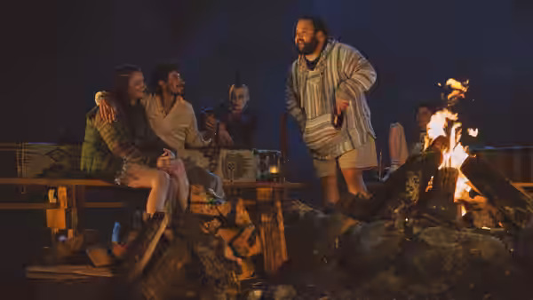 A group gathered around a bonfire at night with one man standing