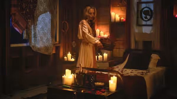 Billy standing in a candlelit bedroom holding a tray