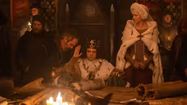 young king at a table with a robed man and a woman in a hall