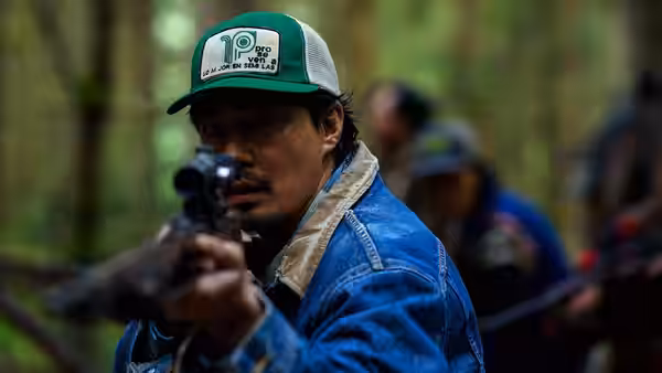Hwang Jung-min as Go Bum-seok aims a rifle through forest undergrowth