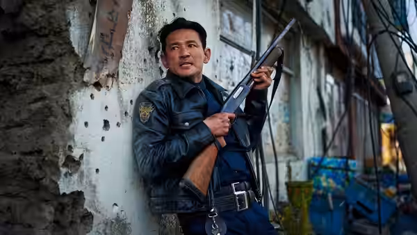 Hwang Jung-min as Go Bum-seok grips a shotgun against a bullet-scarred wall