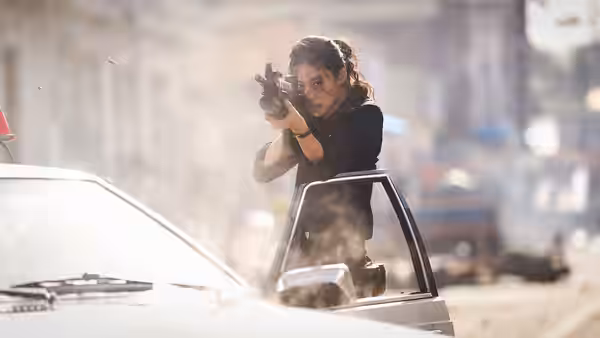 A woman leans from a car door aiming a pistol amid smoke and debris