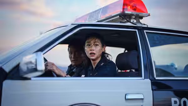 A policewoman drives a patrol car while a male officer sits beside her