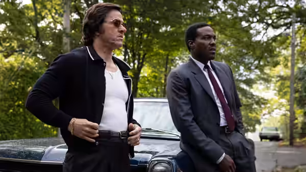 Gregory Scarpa (Mark Wahlberg) and Wayne Strider (Yahya Abdul-Mateen II) stand by a blue car