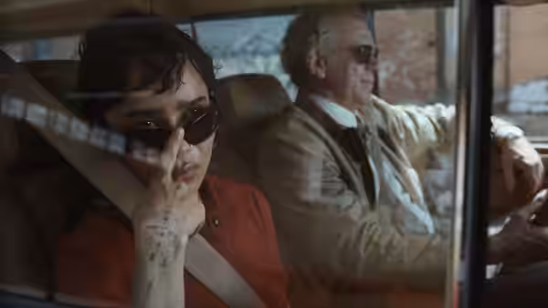 Dark-haired woman gesturing from passenger seat beside an older driver