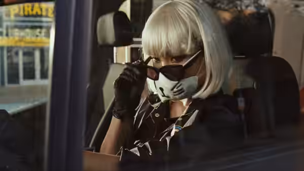 A masked woman in a blonde wig adjusts her sunglasses inside a bank