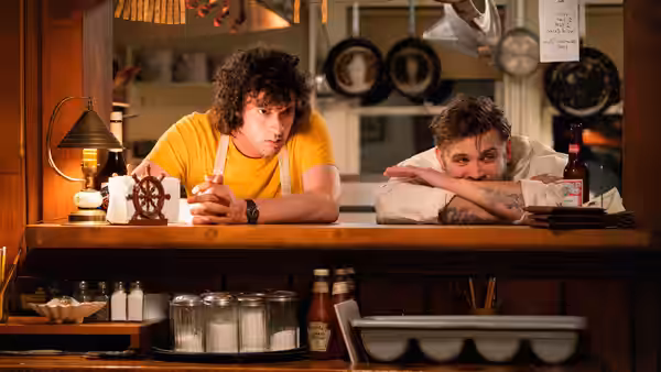Tony (Dominic Sessa) and a man leaning on a wooden bar counter