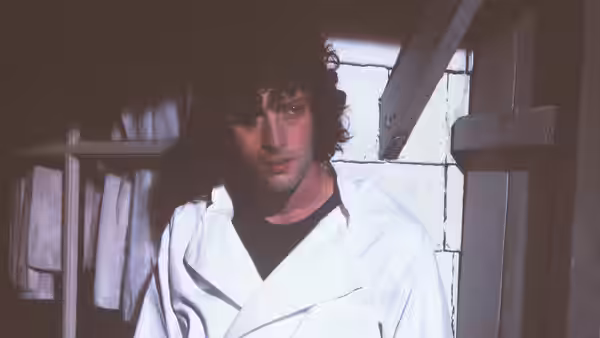 Tony (Dominic Sessa) in a white coat standing in a dim room