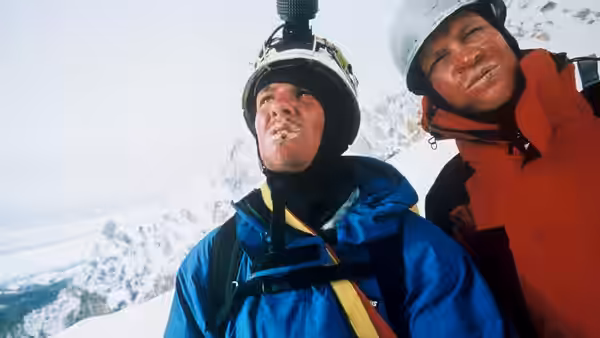 Two climbers in helmets posing together against mountain backdrop
