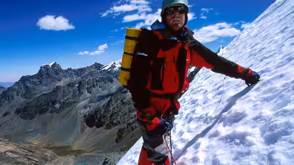 Mountaineer in red jacket standing on snowy slope with yellow pack