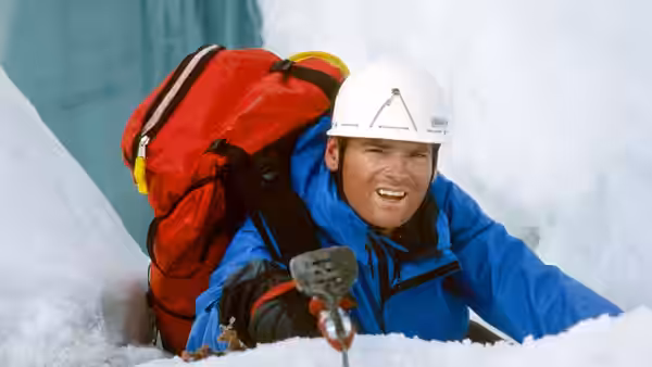 Climber in blue jacket emerging from crevasse with red backpack