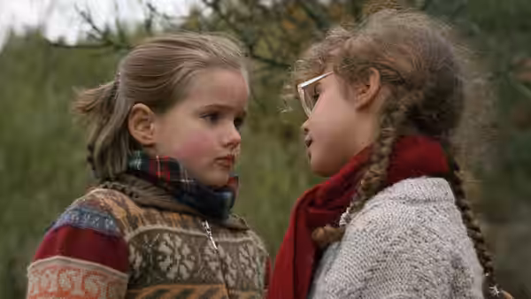 Two young girls face each other outdoors, bundled in sweaters and scarves