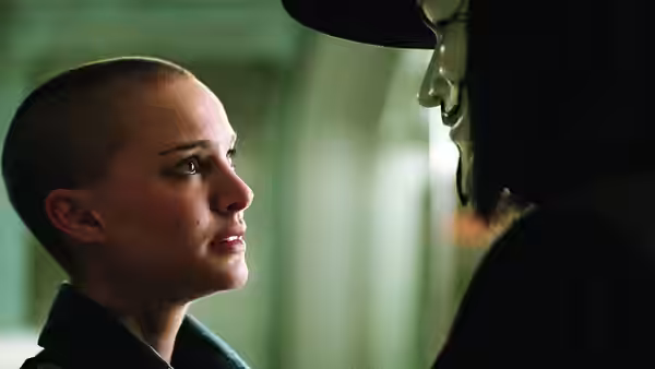 Evey with shaved head stands close to V in a green corridor