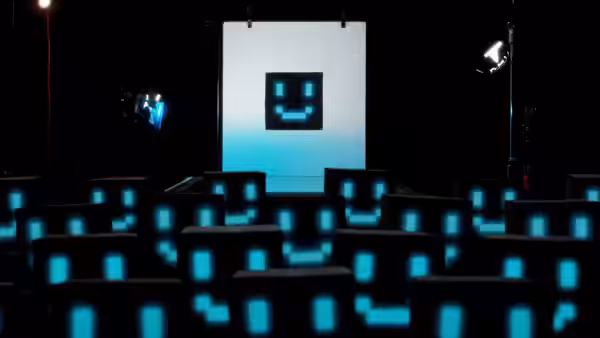 A dark auditorium with rows of glowing blue pixel smiley faces facing a large screen