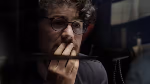 Close-up of a man with glasses and a beard holding fingers near his mouth