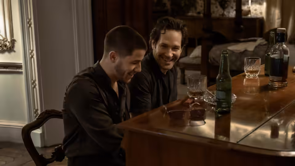 Danny Wilson (Nick Jonas) and Rick (Paul Rudd) smiling over drinks at a table