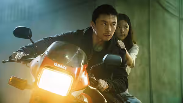 A man drives a red motorcycle through a tunnel with a passenger